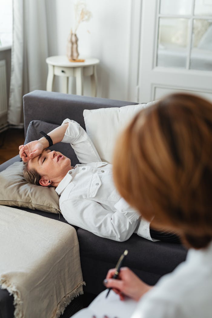 Woman in therapy session relaxing on sofa, attended by therapist in a professional setting.
