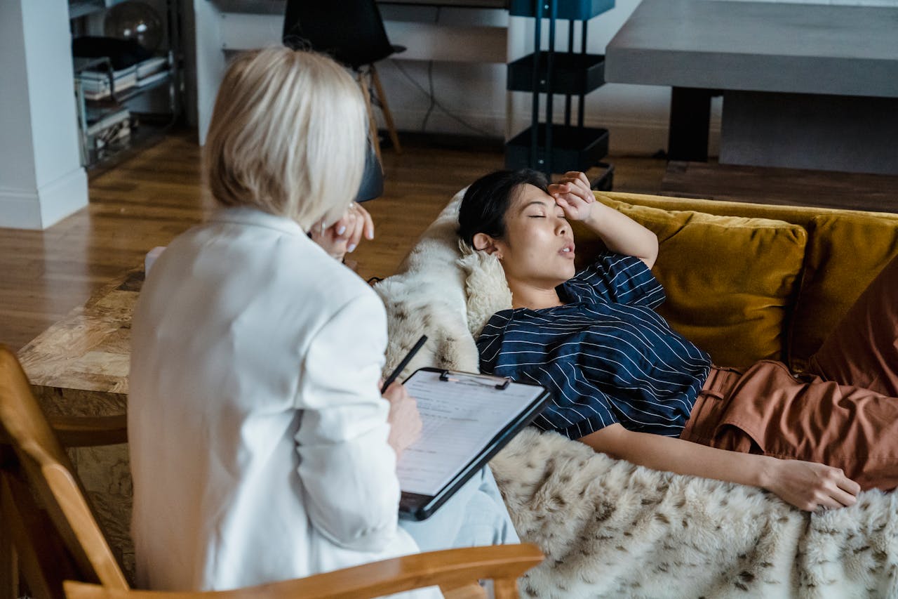 Woman in therapy session lying on couch, discussing emotions with a therapist taking notes.